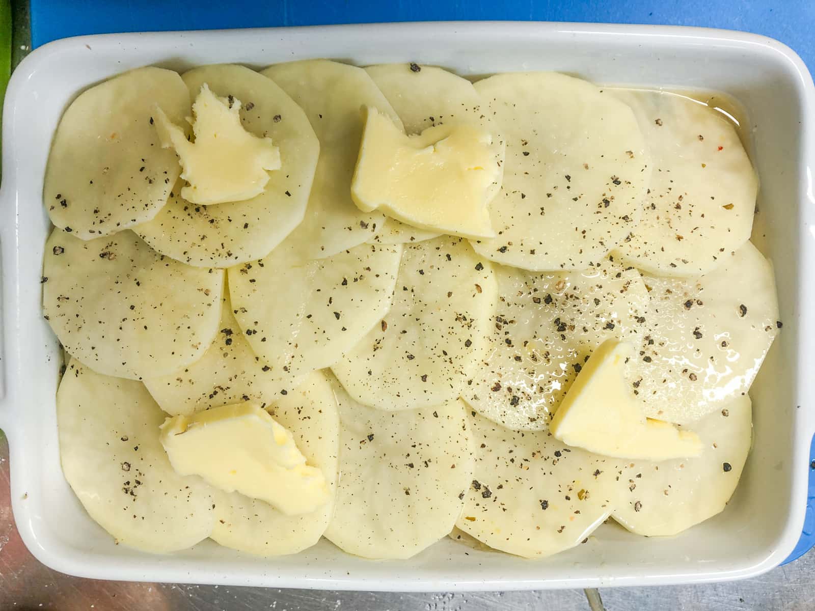 Finishing off a dish of potatoes with lots of salt, fresh black pepper and dotted with salted butter.